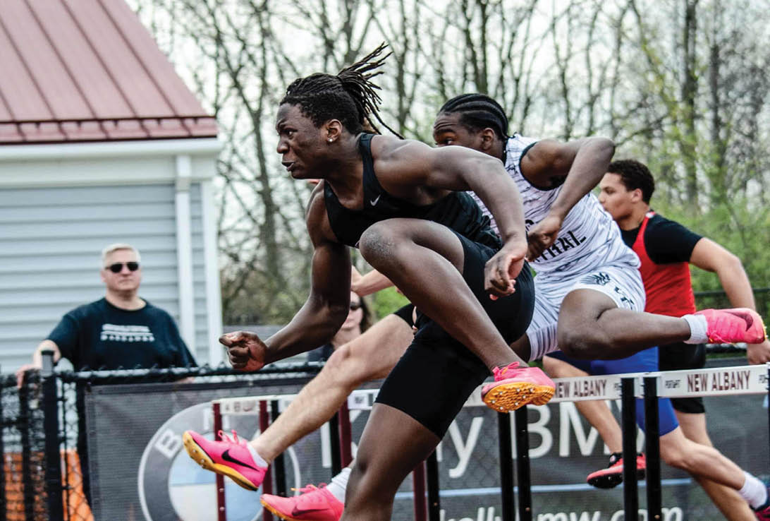 A man wearing a black shirt and pink shoes is jumping over a hurdle. Description generated by AI
