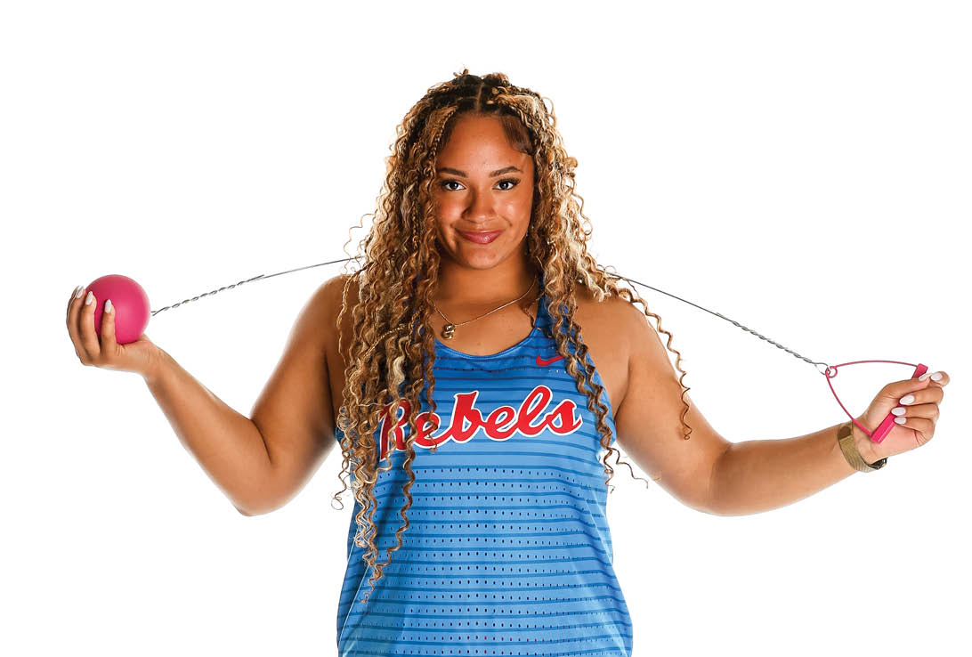 A woman wearing a blue and red shirt and red shorts holding a pink ball. Description generated by AI