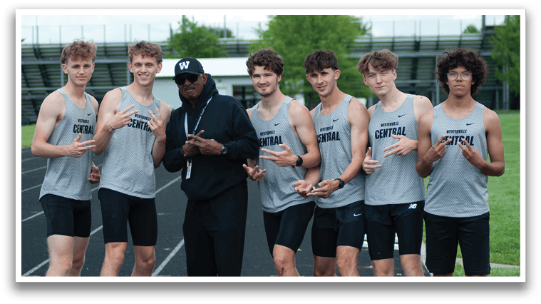 A group of young men wearing grey shirts and black shorts pose for a picture. Description generated by AI