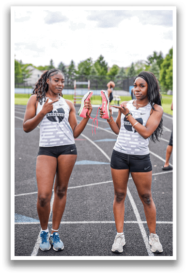 Two women standing on a track holding shoes. Description generated by AI