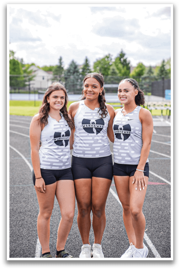Three girls standing on a track. Description generated by AI