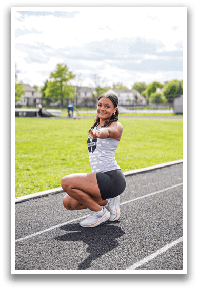 A woman wearing a white and black shirt and black shorts is squatting on a track. Description generated by AI