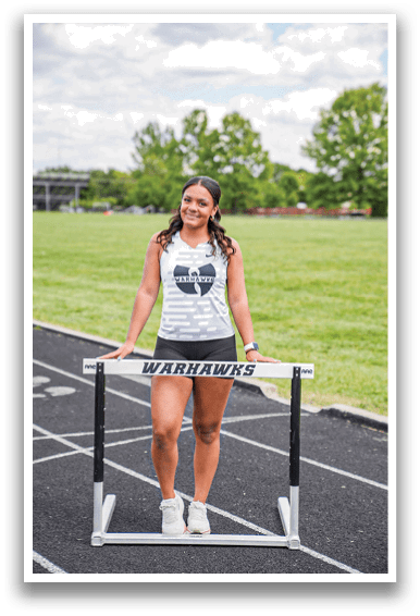 A woman standing on a track with a hurdle in front of her. Description generated by AI