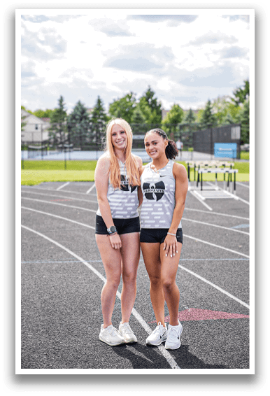 Two women standing on a track. Description generated by AI