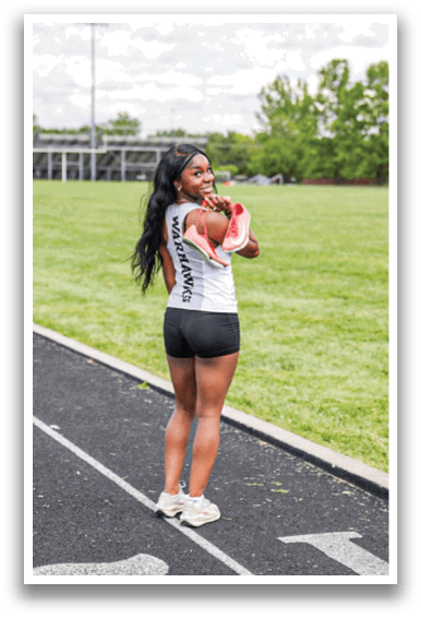 A woman standing on a track with the number 18 on it. Description generated by AI