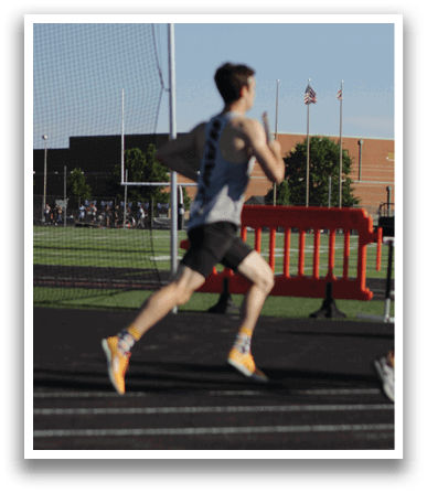 A man running on a track with a red fence in front of him. Description generated by AI