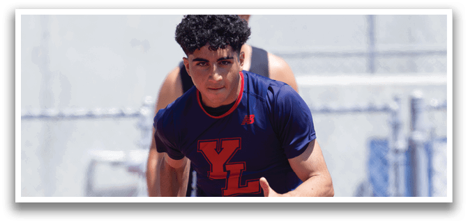 A man wearing a blue and red shirt running on a track. Description generated by AI