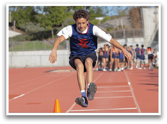 A boy in a blue and red jersey is jumping over an orange cone on a track. AI generated content