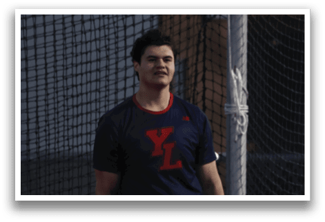 A man wearing a blue shirt and black shorts stands in front of a batting cage. AI generated content