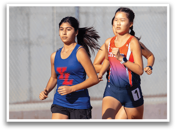 Two girls running on a track, one wearing a blue tank top and the other wearing an orange tank top. AI generated content