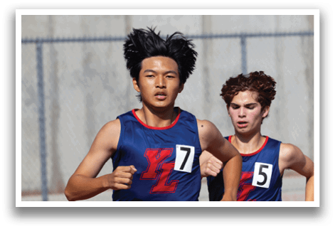 Two young men are running on a track, wearing blue shirts and shorts. They are both wearing numbers on their shirts, indicating they are participating in a race. AI generated content
