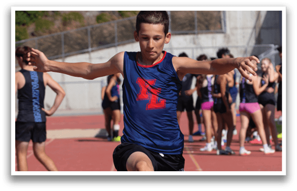 A boy in a blue shirt is jumping over an orange cone on a track. AI generated content
