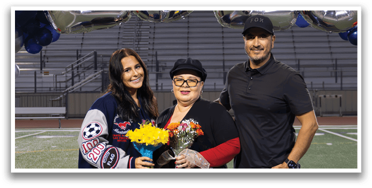 A man and woman stand on a football field in front of a banner that reads “2026". The woman is holding a football. AI generated content