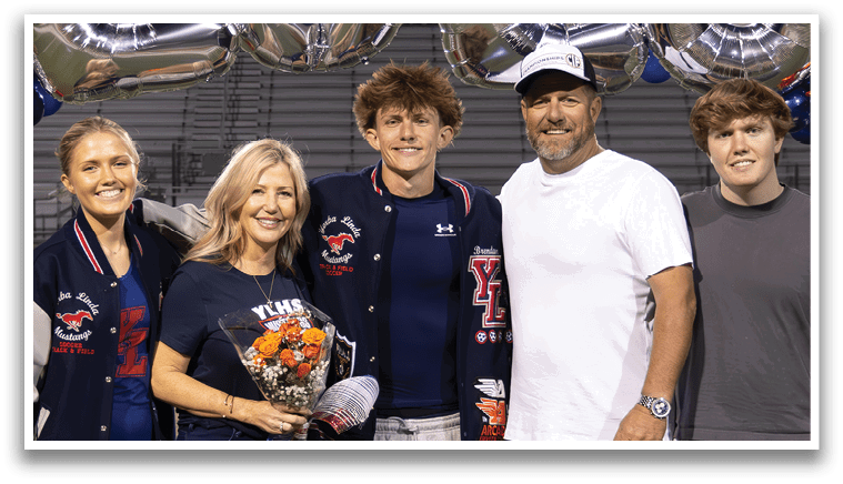A group of four people, two men and two women, pose for a picture in front of a banner that reads “2016." They are standing on a football field. AI generated content