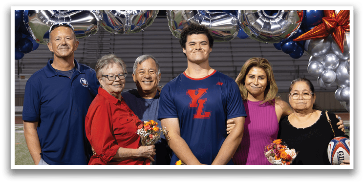 A group of people, including a man and a woman, pose for a picture on a football field. They are standing in front of a banner that reads “2026." AI generated content