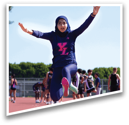 A woman wearing a blue shirt and a head scarf is jumping in the air. Description generated by AI