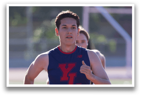 A man running on a track wearing a blue and red shirt. Description generated by AI