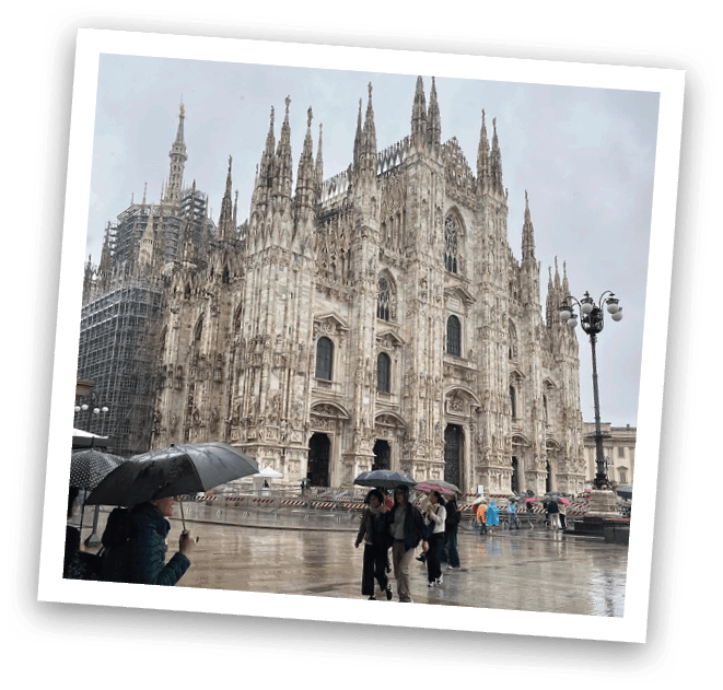 A group of people are walking on a sidewalk in front of a large building with a clock tower. Some of them are holding umbrellas. AI generated content