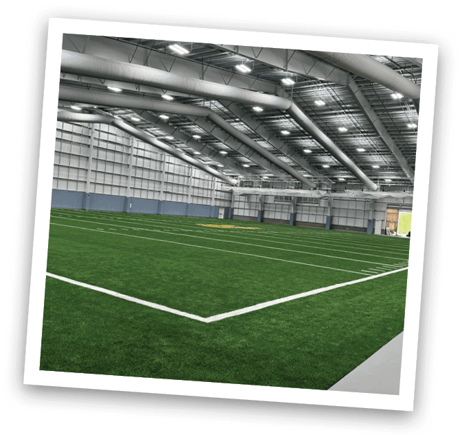 A large indoor sports field with a green turf surface. AI generated content
