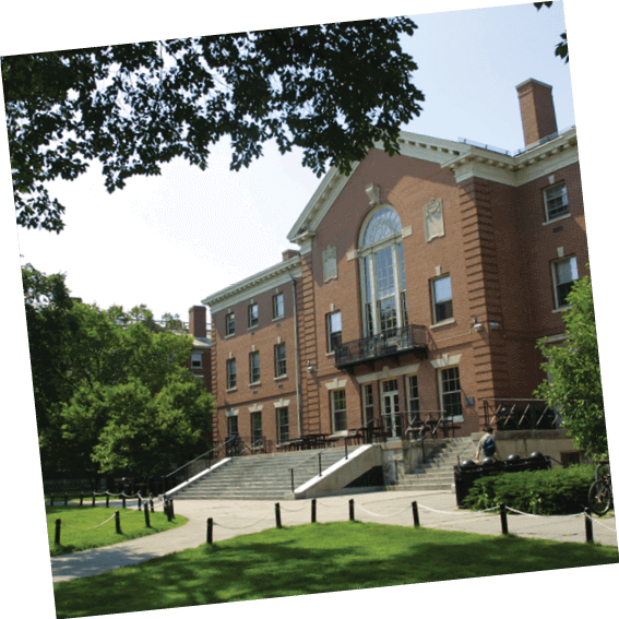 A large brick building with a white roof and a clock tower. The building has a large clock on the side. The building is surrounded by trees and a grassy area. AI generated content