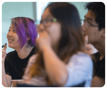 A woman with purple hair is sitting at a table with a man and a woman. She is wearing glasses and has her hand on her face. AI generated content