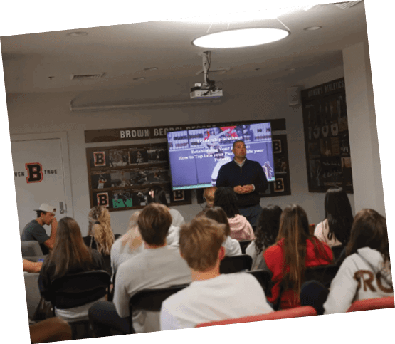 A group of people are sitting in a room, watching a man on a large screen. AI generated content