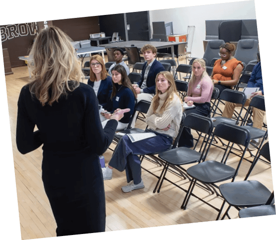 A woman in a black dress is standing in front of a group of people in a classroom setting. AI generated content