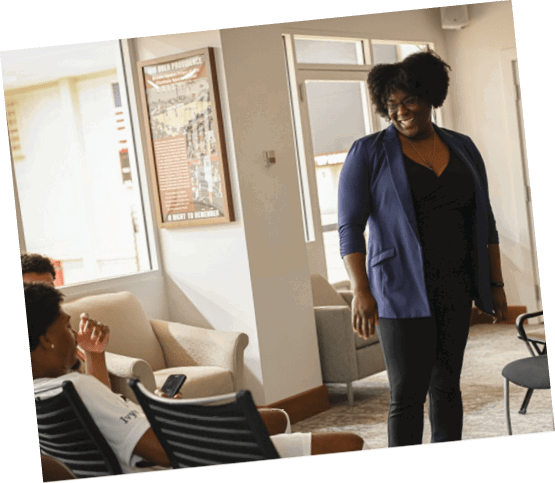 A woman in a blue jacket stands in a room with a group of people sitting on chairs. AI generated content