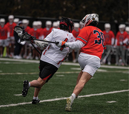 A man in a white jersey is trying to get past another man in an orange jersey. Description generated by AI