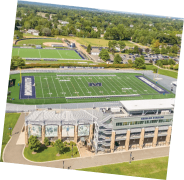 Aerial view of a sports complex featuring a football field with a large “M" logo, a stadium building labeled "Kessler Stadium," surrounding track, and additional sports fields in the background. Description generated by AI