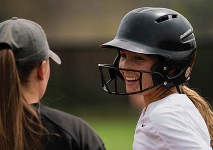 Two girls are talking on a field. One girl is wearing a helmet and a batting glove. AI generated content