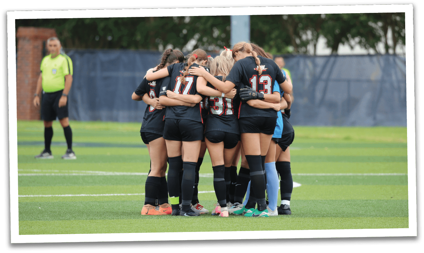A group of female soccer players huddle together on the field, wearing black and red uniforms. AI generated content