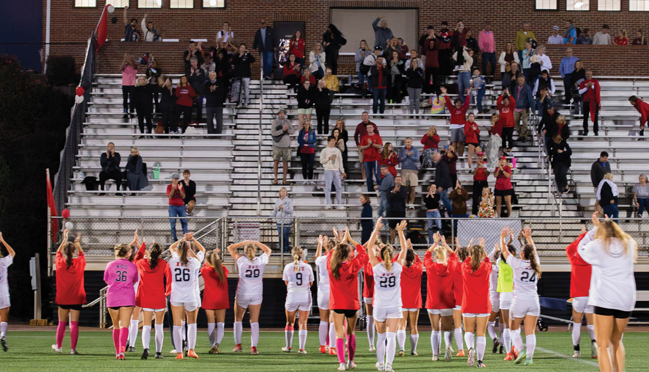 A group of women in red and white uniforms are standing on a field, waving to the crowd. AI generated content