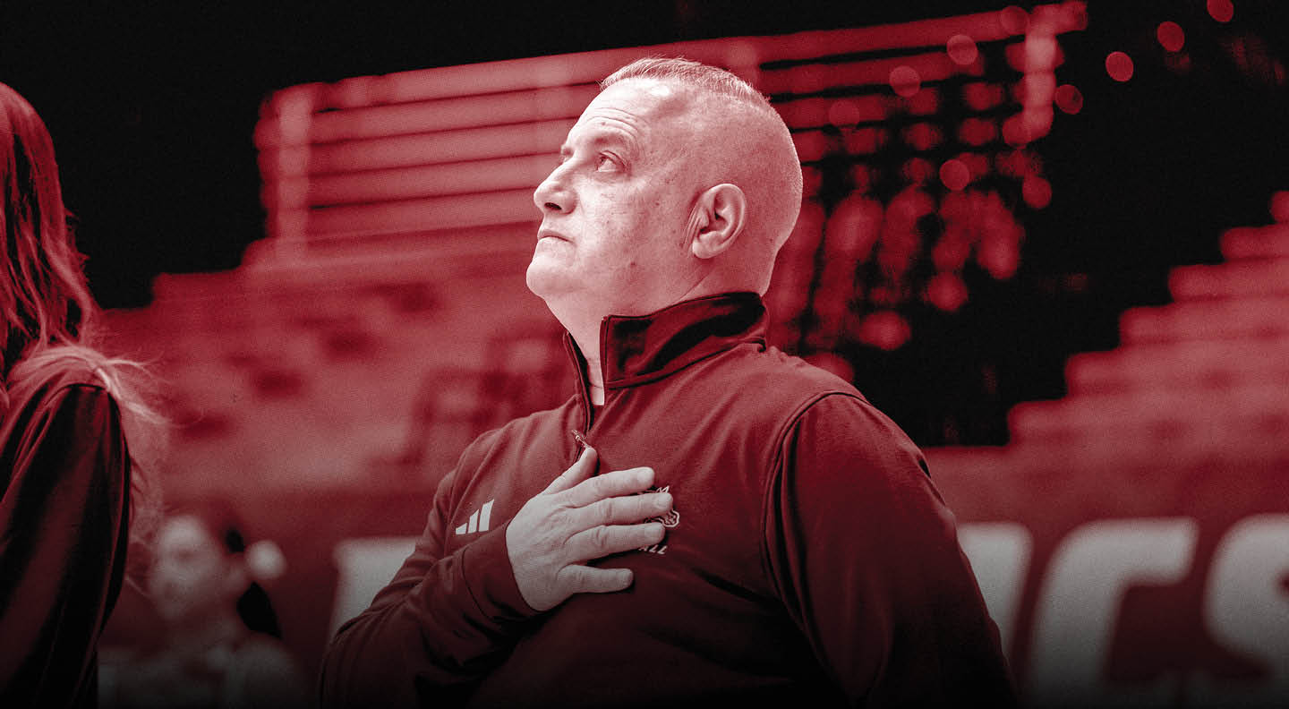 A person wearing a dark jacket stands with one hand over their chest in a setting that appears to be a sports arena. Description generated by AI