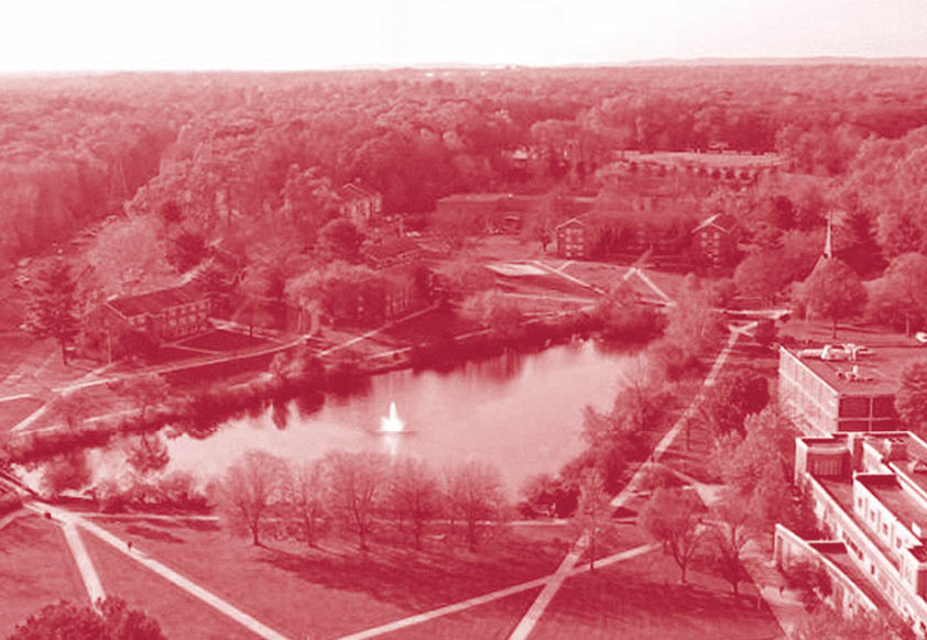 Aerial view of a park-like campus with a central pond featuring a fountain, surrounded by trees, pathways, and multiple buildings. Description generated by AI