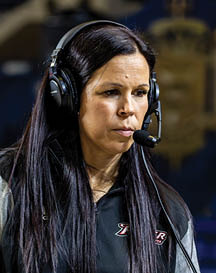 A person with long dark hair is wearing large black over-ear headphones against a blurred background. Description generated by AI