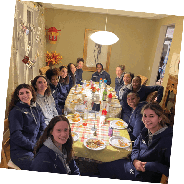 A group of women are sitting around a dining table, posing for a picture. They are wearing blue jackets and are smiling. The table is set with plates, cups, and bottles. AI generated content