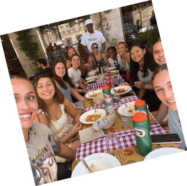 A group of young women are sitting at a table, enjoying a meal together. They are smiling and posing for a picture. There are several cups, bowls, and a fork on the table. AI generated content