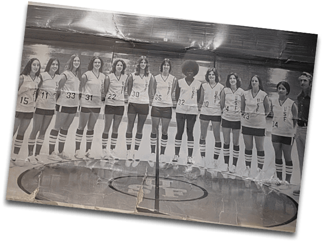 A group of people wearing matching vintage basketball uniforms with knee-high striped socks stand in a line on a gymnasium court. Description generated by AI
