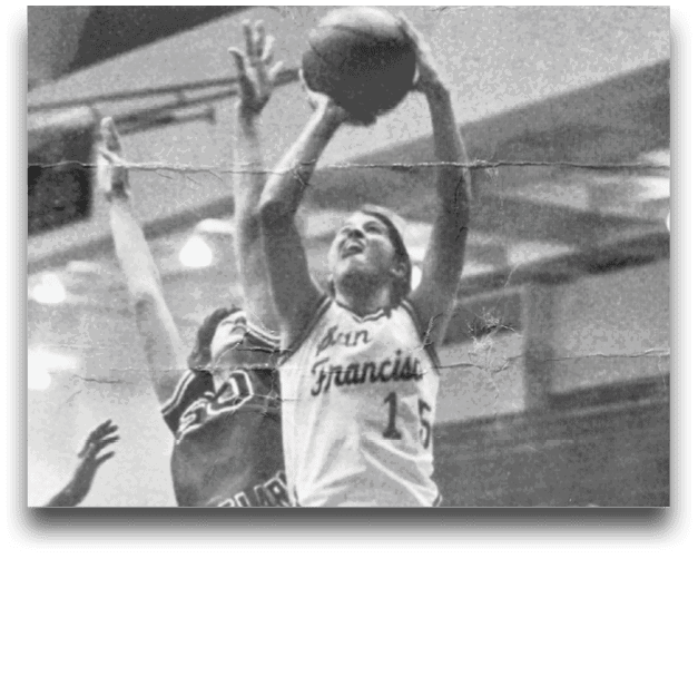 Two people in basketball uniforms are jumping with one holding a basketball preparing to shoot while the other attempts to block the shot in an indoor gym. Description generated by AI