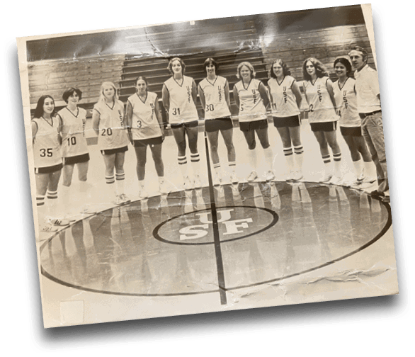 A group of people wearing matching sports uniforms with numbers stand in a line on a gymnasium floor around a large circular logo. Description generated by AI