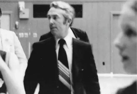 An adult wearing a suit and striped tie is walking indoors with a focused expression. Description generated by AI